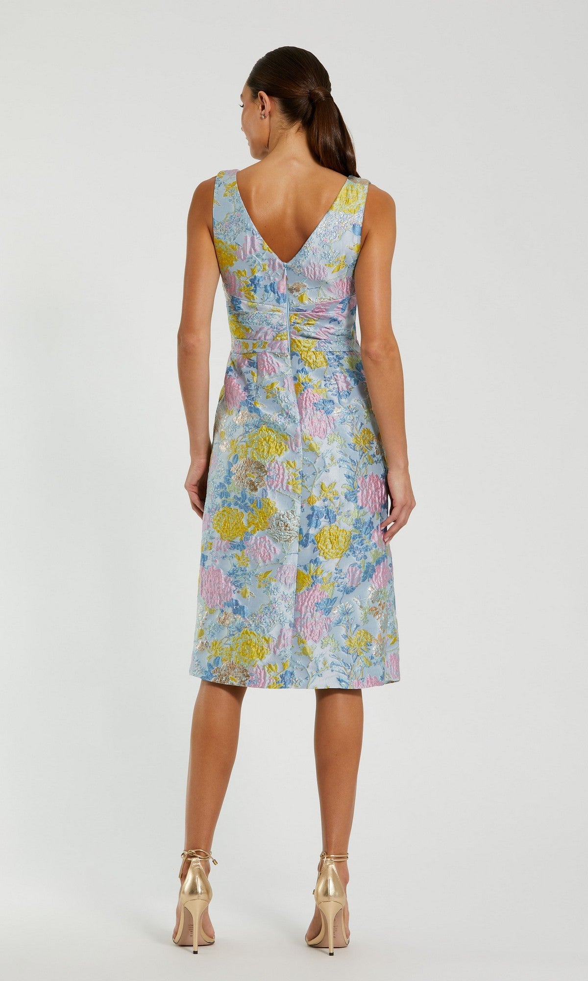 Woman with her back to the camera wears the Mac Duggal 56104 Knee Length Wedding Guest Dress in pastel floral brocade, paired with metallic high heels.